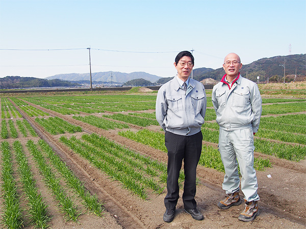 遠くに宝満山を望む圃場で並ぶ田中さんと甲斐さん